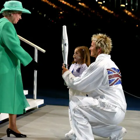 PA Media David Beckham and Kirsty Howard hand the Queens Jubilee Baton to Queen Elizabeth II after it's final leg around the city of Manchester stadium, at the opening ceremony of the Commonwealth Games.