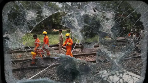 EPA Rescue workers walk along the tracks, seen through a shattered window from the carriage