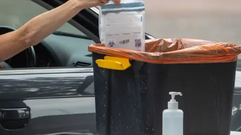 PA Media A person places a completed coronavirus test into a collection bin