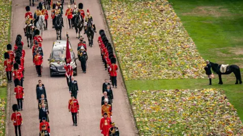 PA Media Emma, the monarch's fell pony, standing besides floral tributes as the Ceremonial Procession of the coffin of Queen Elizabeth II arrived at Windsor Castle