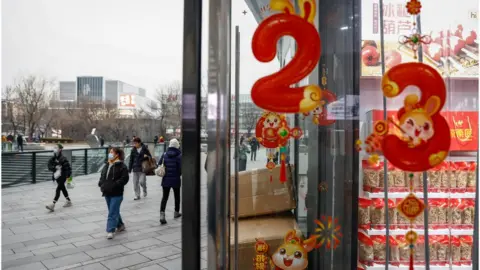 MARK R CRISTINO/EPA-EFE/REX/Shutterstock People walk past Lunar New Year decor in China