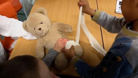 A boy putting a bandage on a teddy bear's leg