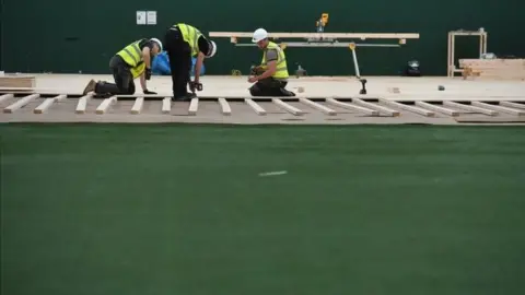 PA Media Workers lay flooring during the construction of a field hospital at Llandarcy sports academy in Neath