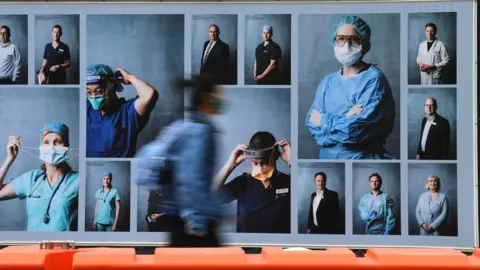 EPA Person wearing a mask walks past a billboard in Melbourne featuring healthcare workers