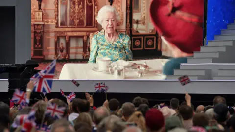 PA Media The Queen and Paddington Bear on a big screen, with people waving union flags in the foreground