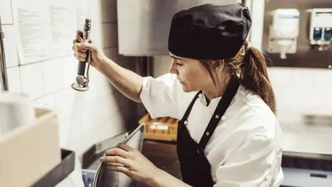 Getty Images Woman washing up in a commercial kitchen