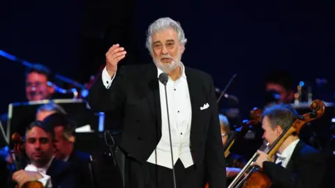 AFP Placido Domingo singing on stage with an orchestra behind him