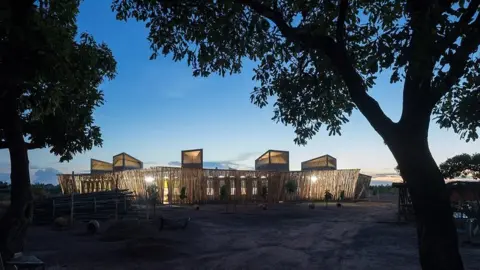 Iwan Baan Lycée Schorge Secondary School at night. There are light on in the building and trees in the forefront of the picture.