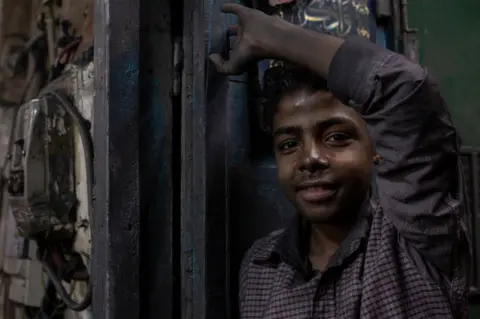 MAHMOUS ELKHWAS/GETTY IMAGES A boy with sooted hands stands at the doorway to an aluminium workshop.