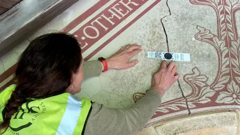 Sally Strachey Historic Conservation A women holding up a sticker to a crack in plasterwork