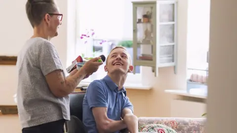 Getty Images A young man with Cerebral Palsy is helped by a carer