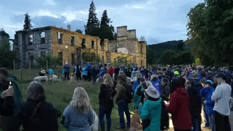 dugs and owners outside the ruined house