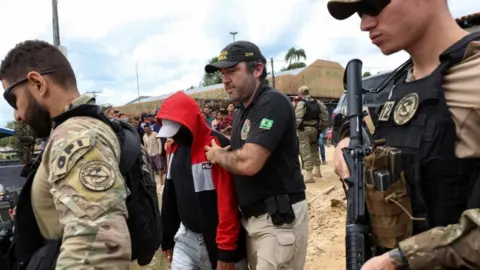 Reuters Federal police officers in Brazil escorted a man accused of being involved in the disappearance of Dom Phillips and Bruno Pereira. 15 June 2022.