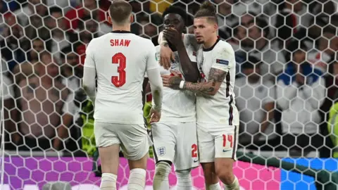 Getty Images Bukayo Saka is comforted by teammates are missing his penalty