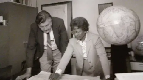 Supplied Gladys West in an office working with a male colleague