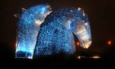 PA Media The Kelpies in Falkirk are lit up in blue