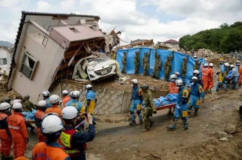 EPA Police and Ground Self-Defense Force's rescue workers carry a victim away after they were killed by a landslide caused by heavy rains in Kumano, Hiroshima Prefecture, Japan