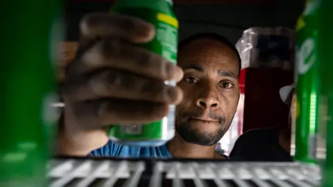 BBC/Shiraaz Mohamed Mulugeta Negash taking a can from a fridge in his shop in Alexandra township, Johannesburg, South Africa