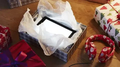 Getty Images A tablet is being opened from a Christmas gift box, with more gifts seen nearby
