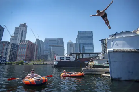 Victoria Jones / PA Wire A man dives into water in the London Docklands, as two other men in inflatable boats watch