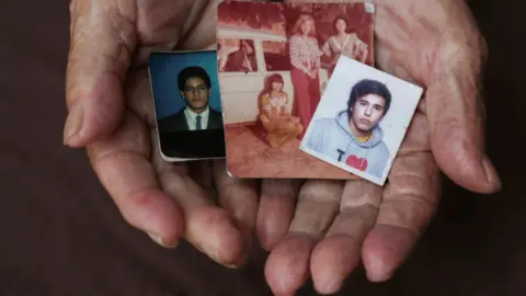 Caritas A close-up of María Teresa Jimenez's hands holding pictures of her children