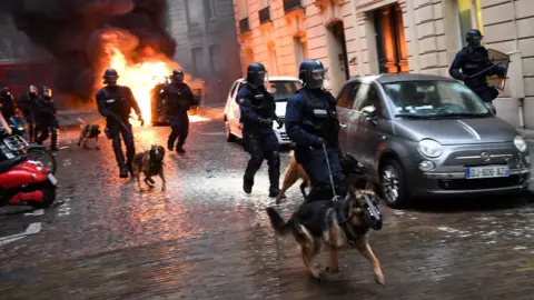 AFP Riot police run next to a car set on fire during a protest of Yellow vest (Gilet Jaune) against rising costs of living they blame on high taxes on December 8, 2018