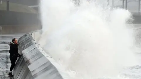 Getty Images A girl looking as high waves crash into a barrier in a storm