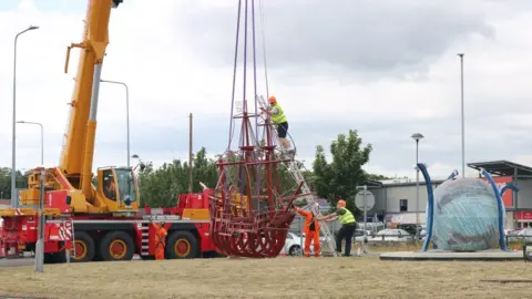 A crane lowers the sculpture