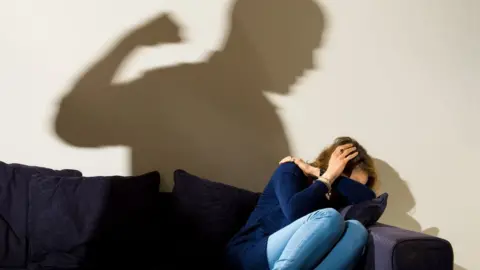 PA Image showing silhouette of a man with a clenched fist threatening a frightened woman (posed by models)