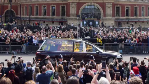 Getty/SOPA Images Crowds line the streets as the Queen's hearse drives past