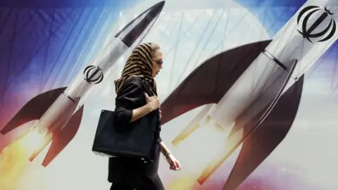 woman walks past propaganda in Tehran