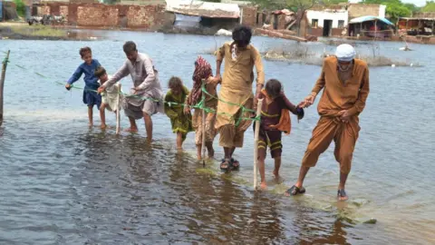 EPA-EFE/REX/Shutterstock People wade through a flooded area following heavy rains in Sanghar District, Sindh province, Pakistan, 28 August 2022