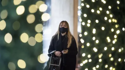 PA Media A woman wearing a face mask, with festive lighting on trees in the foreground