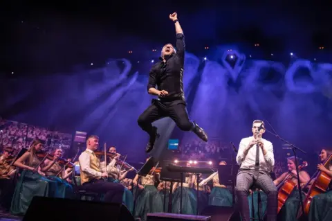 CBoI Conductor Greg Beardsell leaps in the air as the Cross-Border Orchestra of Ireland perform behind him