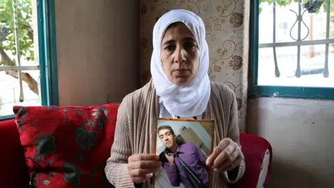 YOAV LEMMER/AFP via Getty Images Image shows woman holding up picture of Hisham al-Sayed