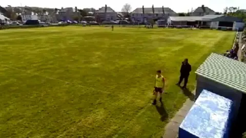 Football pitch with a man in a black coat and a linesman on the side