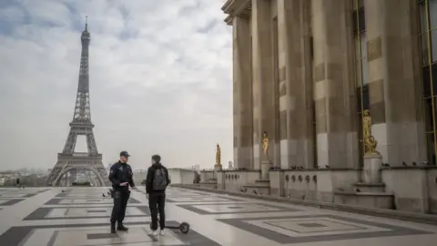 Getty Images Police officers question a scooter rider travelling near the Eiffel Tower hours after a government enforced quarantine on March 17, 2020 in Paris, France