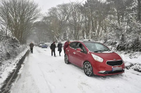 PA People push cars along the A30 near Land's End