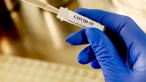Getty Images A gloved hand with a Covid-19 test