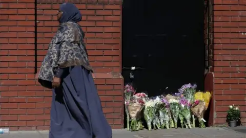AFP Woman passes flowers laid in Finsbury Park