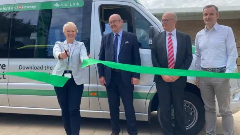 Four people and a ribbon being cut in front of a minibus