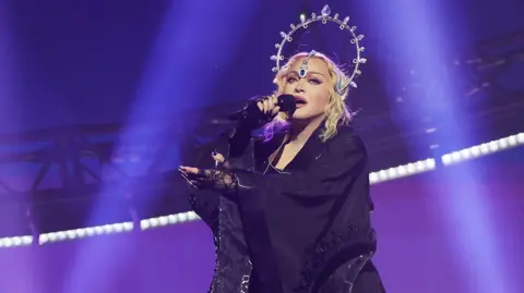 Getty Images Madonna sings into a microphone while performing during the opening night of The Celebration Tour at The O2 Arena on October 14, 2023 in London, England