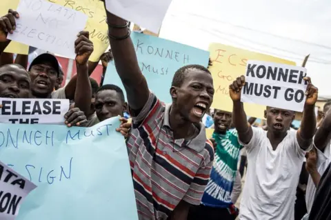 John Wessels/AFP Protesters hold up banner saying "Konneh must go" and other slogans.