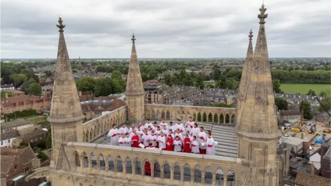 PA Media The St John's choir performs on the top of the chapel's tower