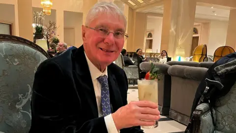 Handout Image of Eric Woods. He is holding up a drink and smiling at the camera.