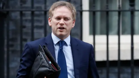 Getty Images Britain"s Transport Secretary Grant Shapps leaves number 10, Downng Street in central London on March 17, 2020. - Britain stepped up its response to coronavirus, recommending household isolation, home-working and an end to mass gatherings to try to stem an accelerating outbreak.