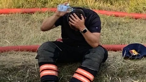 Cambs Fire and Rescue Fireman pouring water on his head