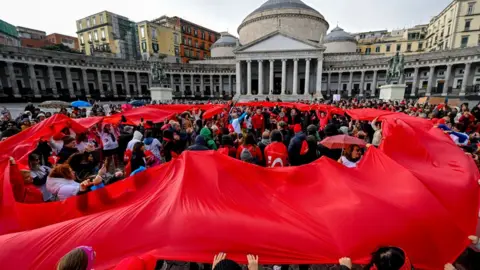 EPA A large crowd of protesters in Naples holding a large red cloth