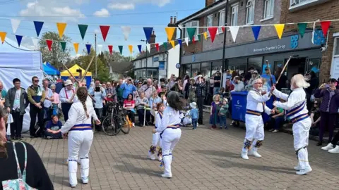 Joanna Ramsay Horbury/Downton Cuckoo Fair Morris dancers at the Downton Cuckoo Fair, with a crowd around them and colourful bunting.