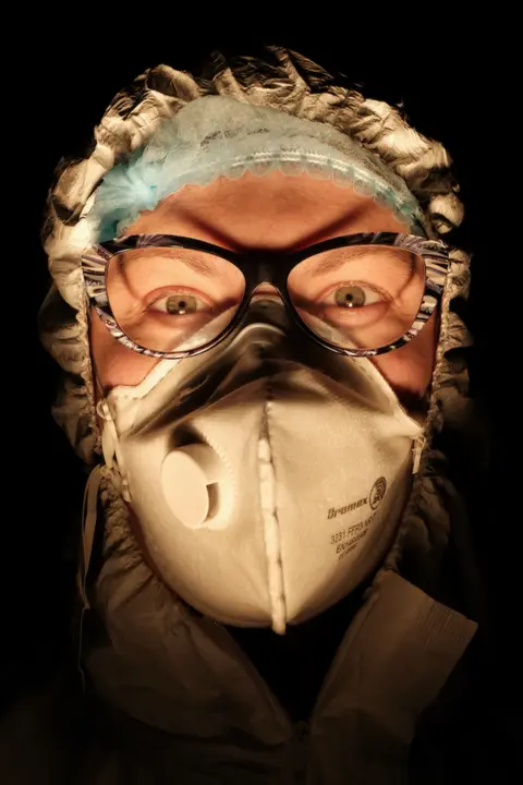 Paolo Miranda A female nurse wearing a face mask with a dark background behind her